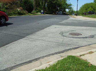 Photo shows the same street looking to the right.  We are standing on the corner of another street, and the main street continues slightly uphill and crests about 50 feet away and disappears down the other side of the hill.